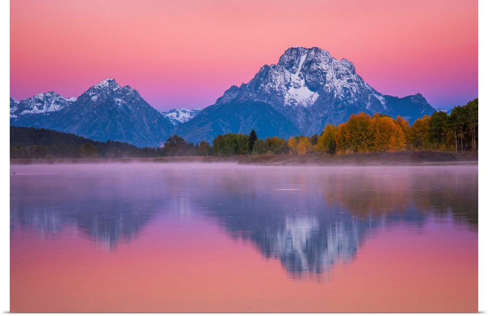 Snow-capped mountains under a pink sunset sky reflected in a lake.
