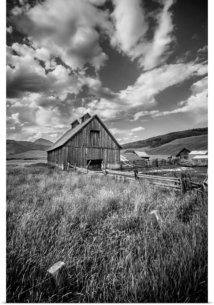 Black and white photograph of farmland with a barn in the center and contrasting clouds in the sky.