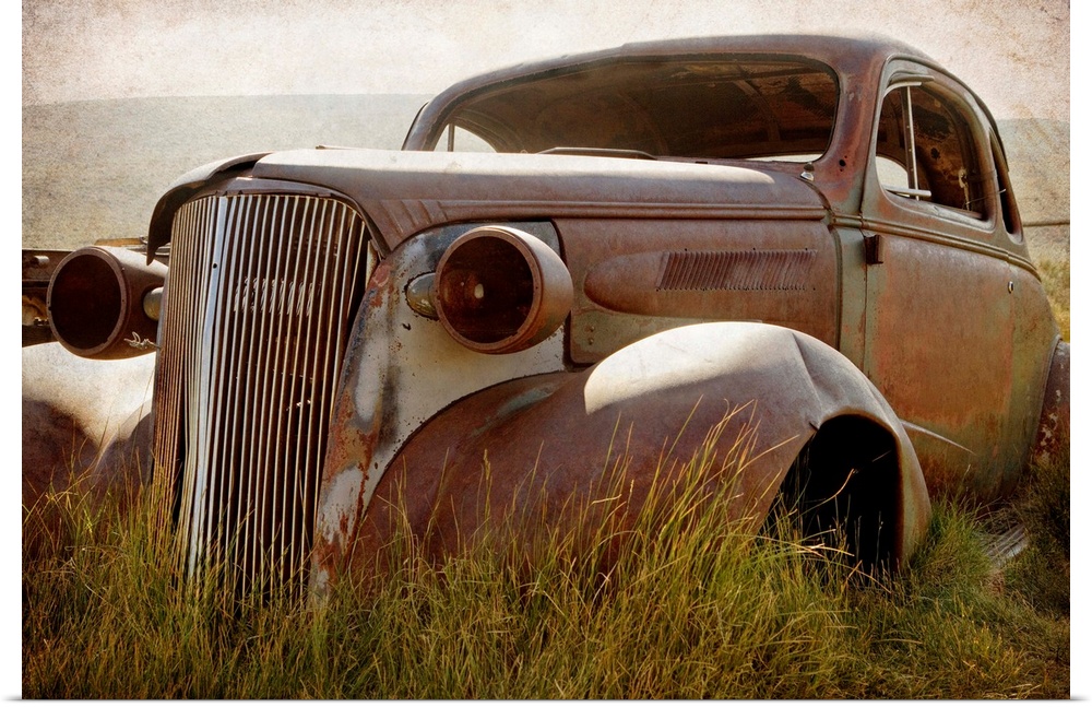 Photograph of a broken down and beat up vintage car in a junkyard.