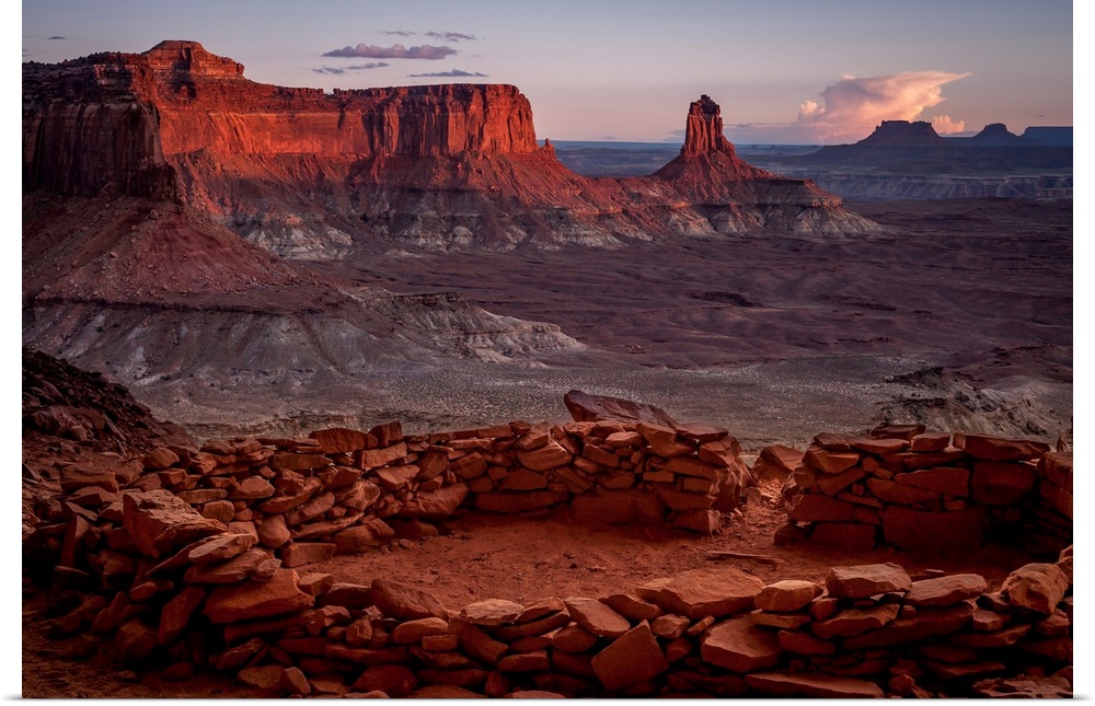 Landscape photograph of stacked rocks creating a circle with canyons in the background at sunrise.
