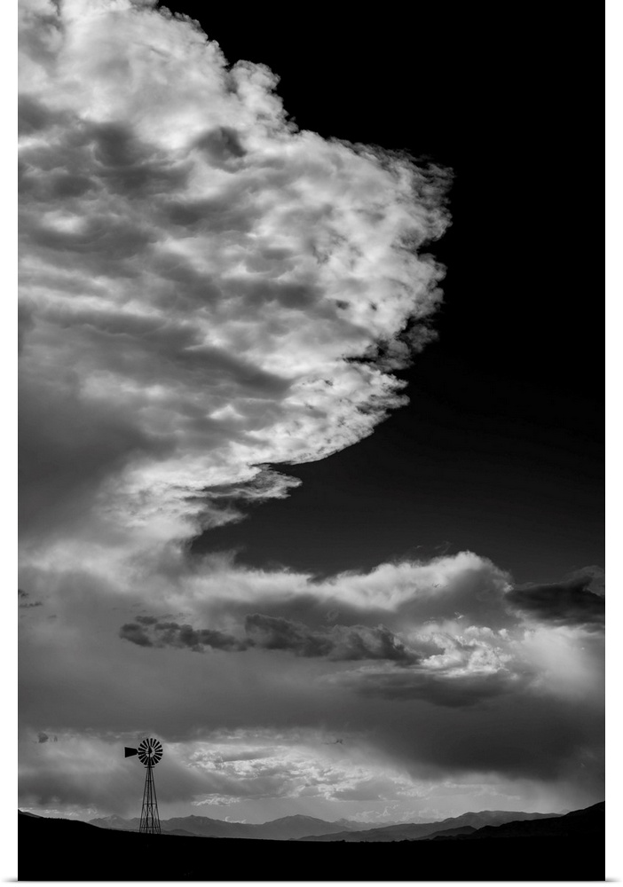 Black and white photograph of a beautiful cloudy sky with a windmill silhouette in the distance.
