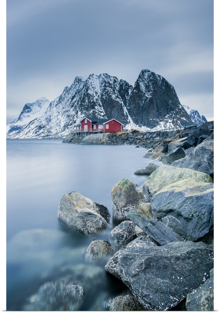A photograph of a Norwegian red cabin with gray mountain boulders all around.