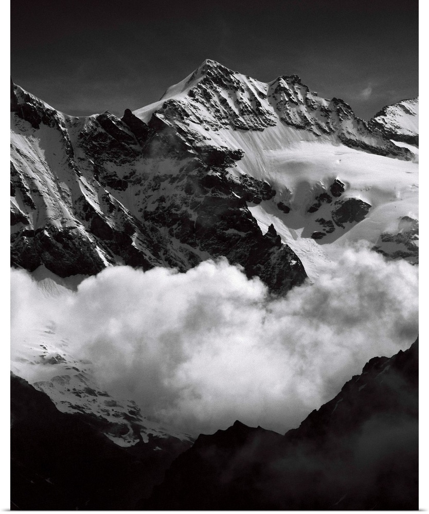 Black and white photograph of mountain peaks surrounded by rolling clouds.