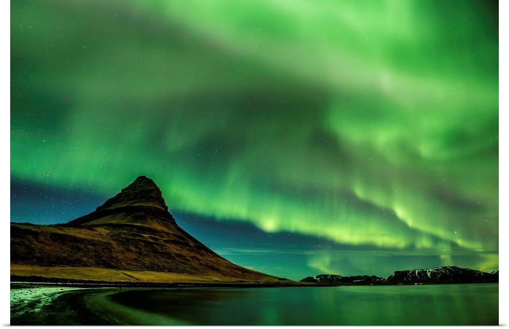A photograph of an Icelandic landscape with a mountain peak seen under the northern lights illuminating the sky.