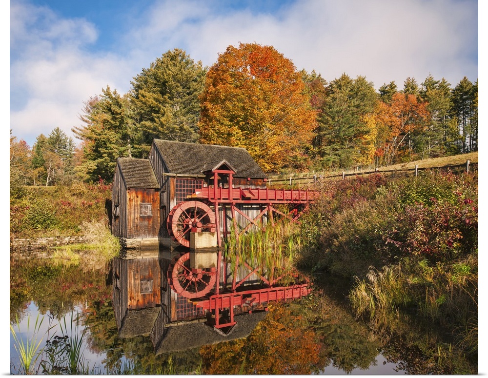 A photograph of a red water mill in the middle of a forest in autumn foliage.