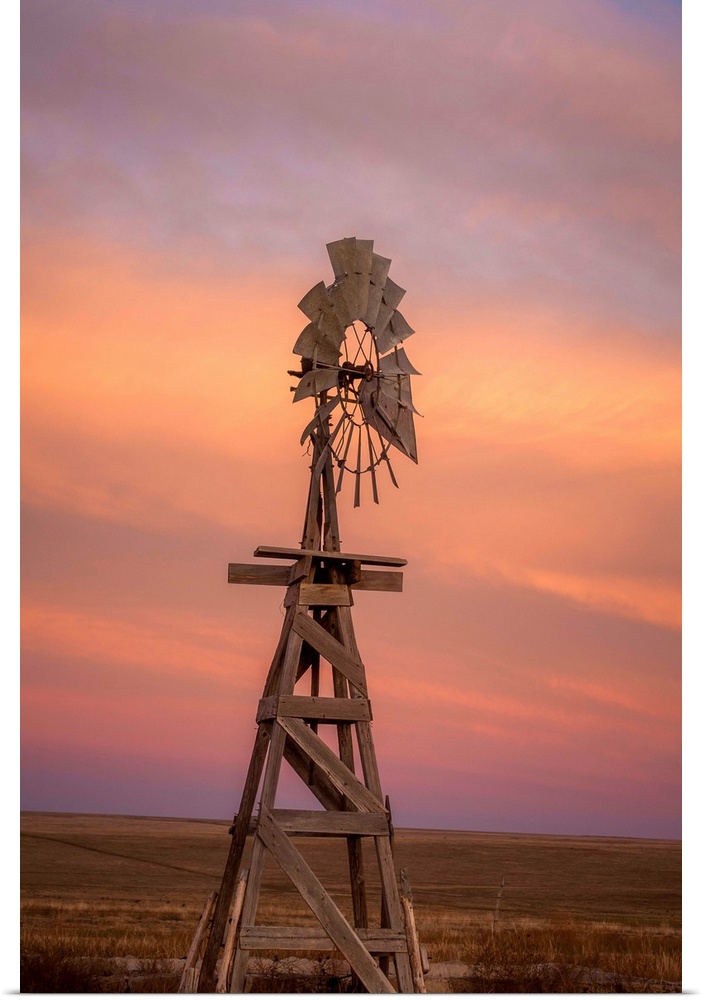 Photograph of a wooden windmill in the middle of a field at sunset.