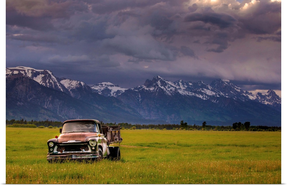 Landscape photograph of a yellow-green field with an old rusted truck and snow capped mountains in the background.
