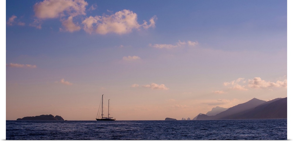 Photograph of a single sailboat in the middle of the ocean with silhouettes of mountains in the distance.