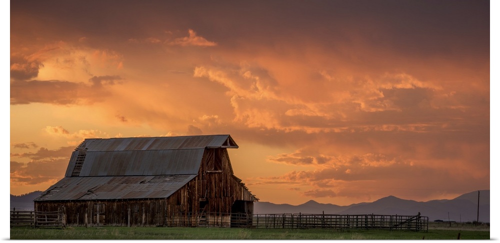 A photograph of an old barn under illuminated clouds of a sunset.