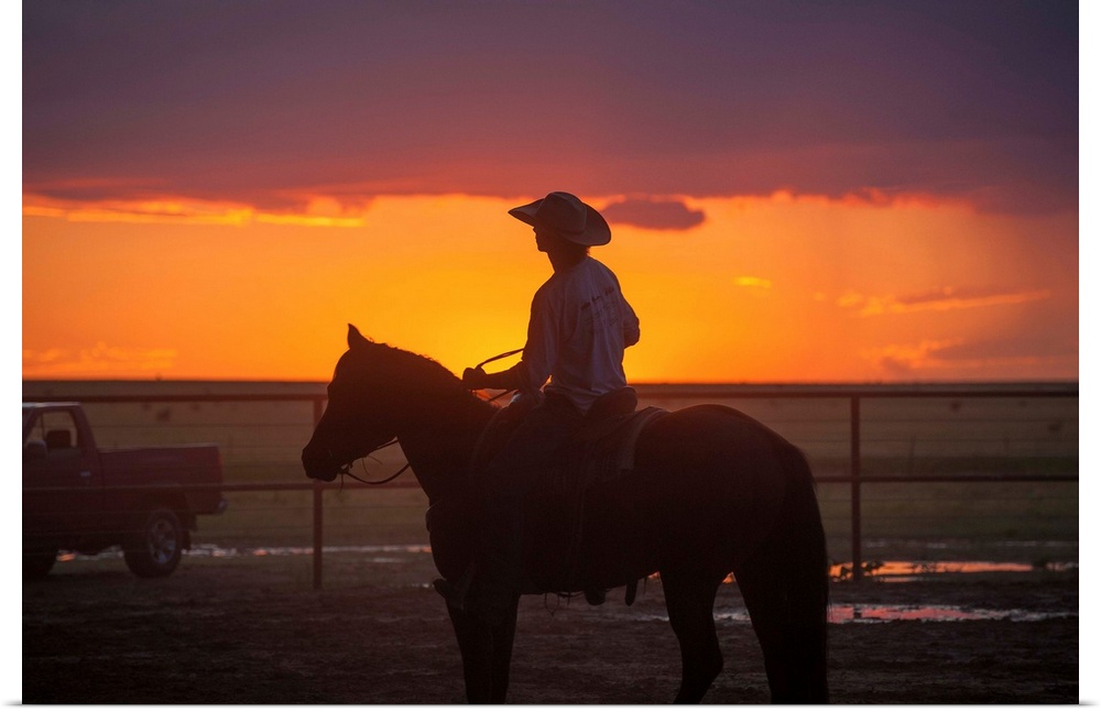 Silhouette photograph of a cowboy on horseback with a beautiful purple and orange sunset in the background.