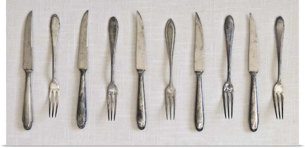 Photograph of a row of silver antique forks and knifes on a linen cloth.