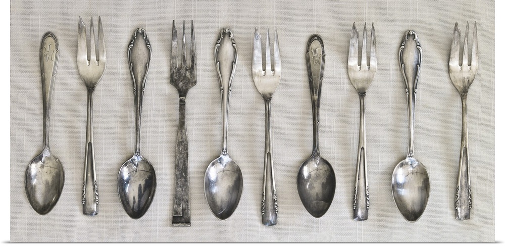 Photograph of a row of silver antique forks and spoons on a linen cloth.