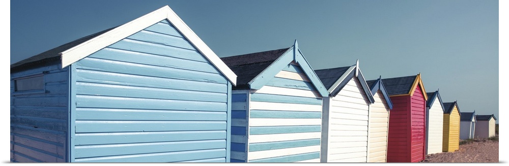 A panoramic image of a long line of colorful beach huts on a clear day.