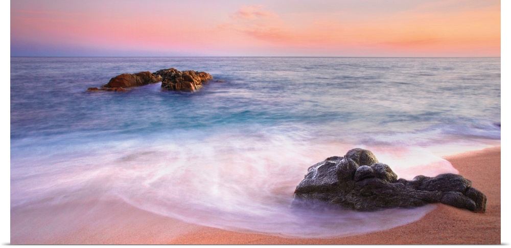 Panoramic image of gentle waves on a rocky seashore with a vibrant pink sunset.
