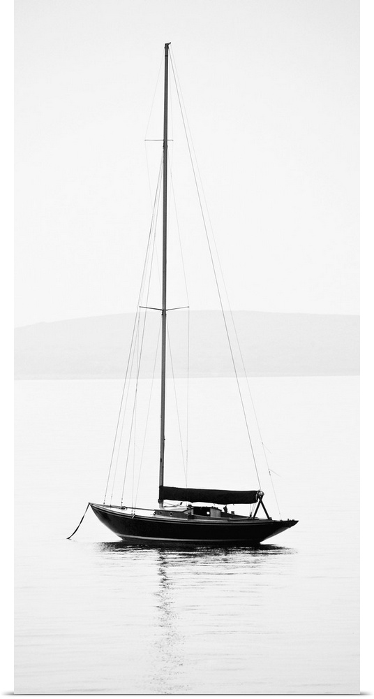 Black and white photograph of a sailboat with its sail down on calm water.