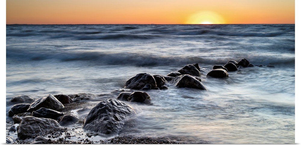 Photograph of a line of rocks in the surf of a beach during sunset.