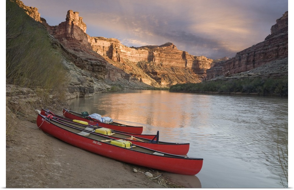 USA, Utah, Canyonlands National Park. Three red canoes rest on bank of Green River.