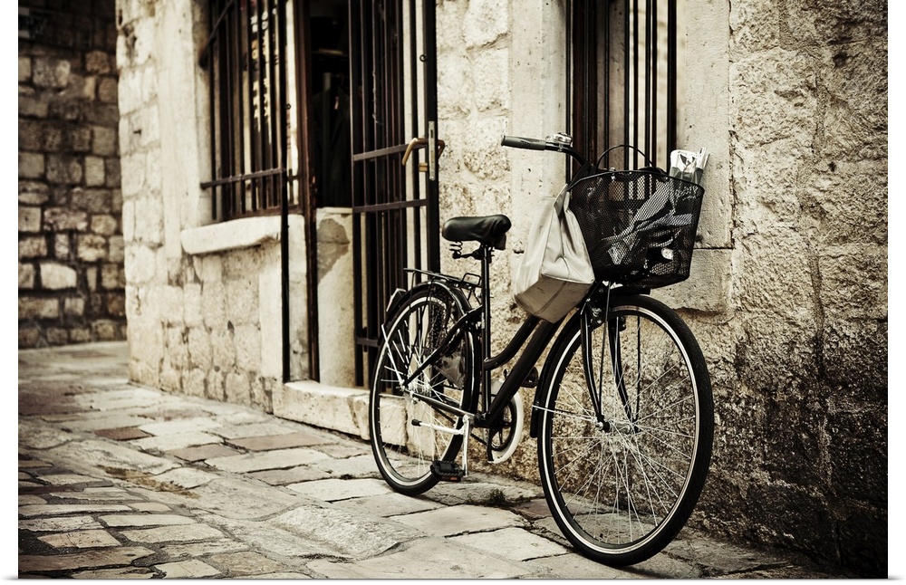 Old bicycle with basket and shopping bag parked in the narrow cobble street.