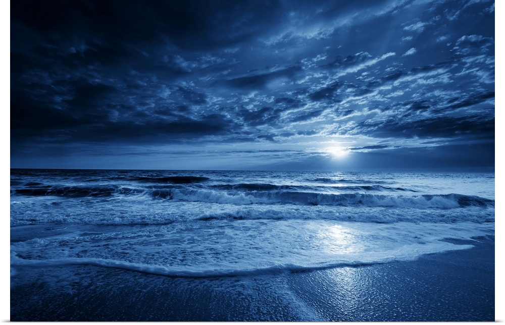 This is a photographic illustration of a beautiful midnight-blue ocean moonrise with dramatic sky and rolling waves.