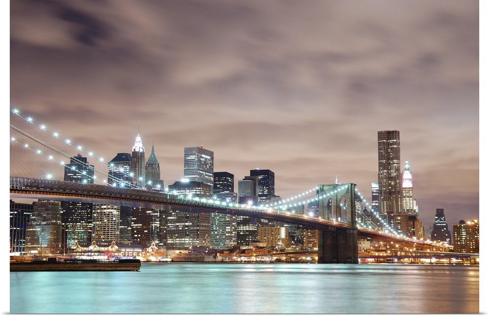 Panoramic view of Manhattan with Brooklyn Bridge at night and skyscrapers illuminated over Hudson River.