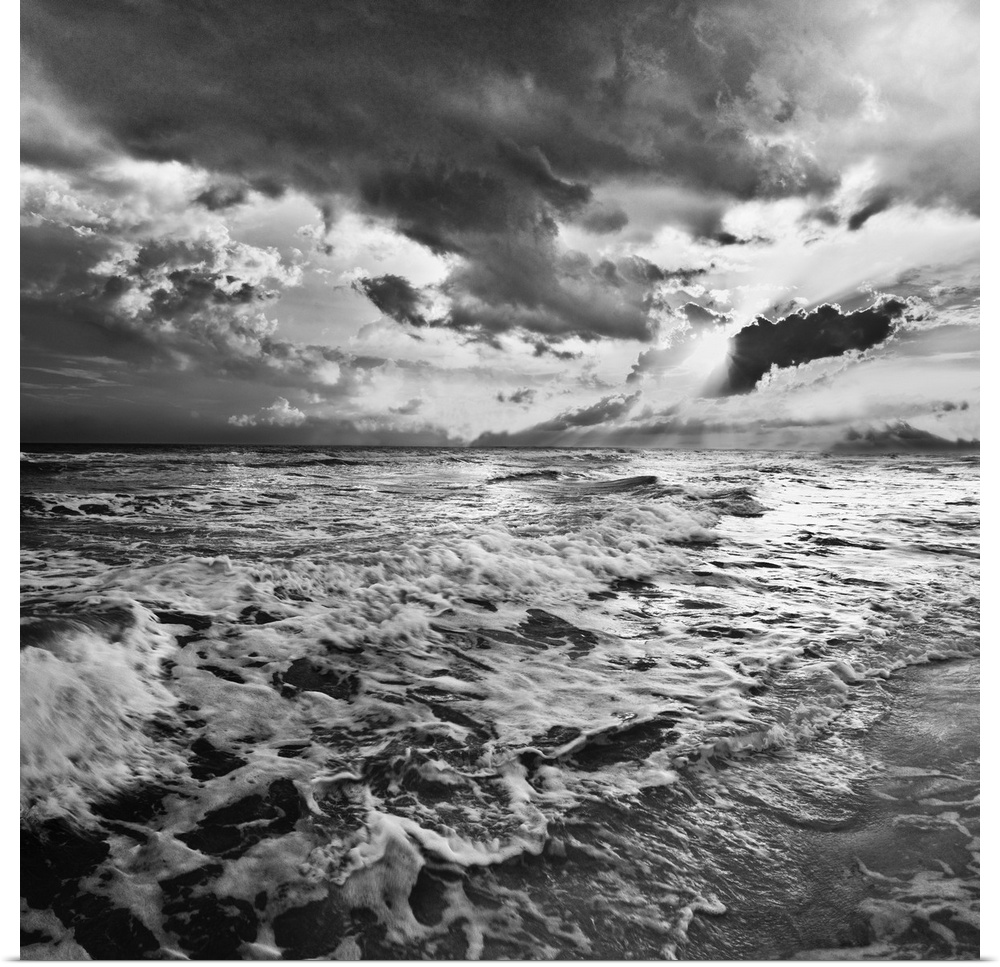 A black and white image of the sea with crashing waves on the beach.