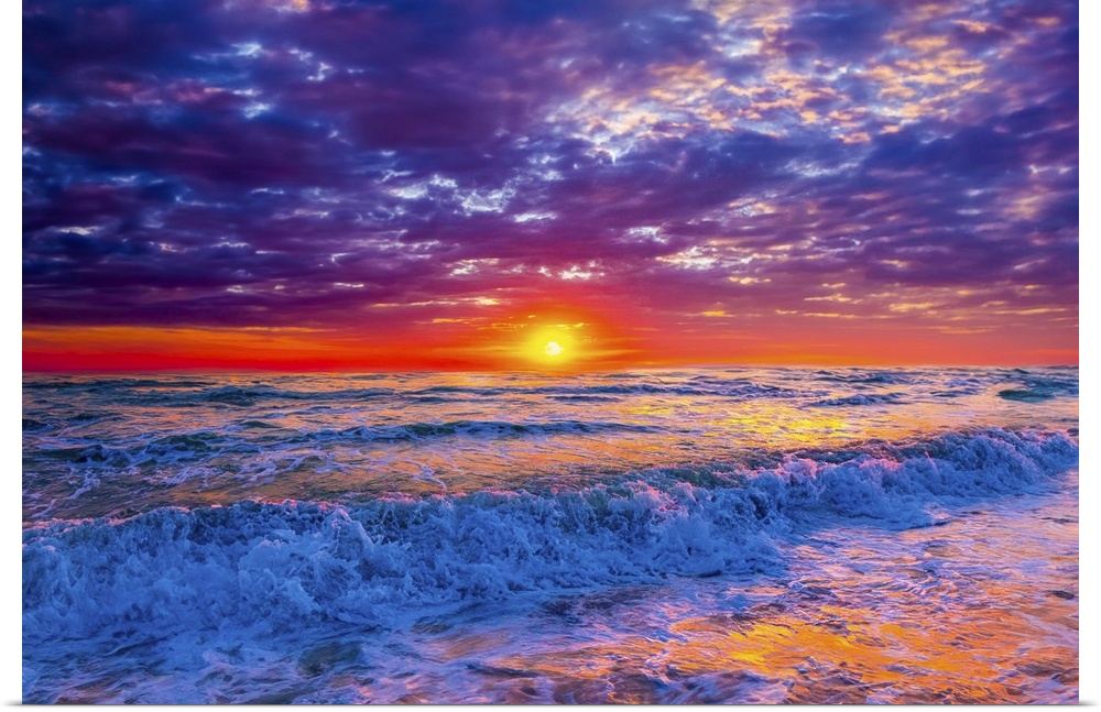 Blue ocean waves crash onto the beach beneath a red, lavender, and purple sunset.