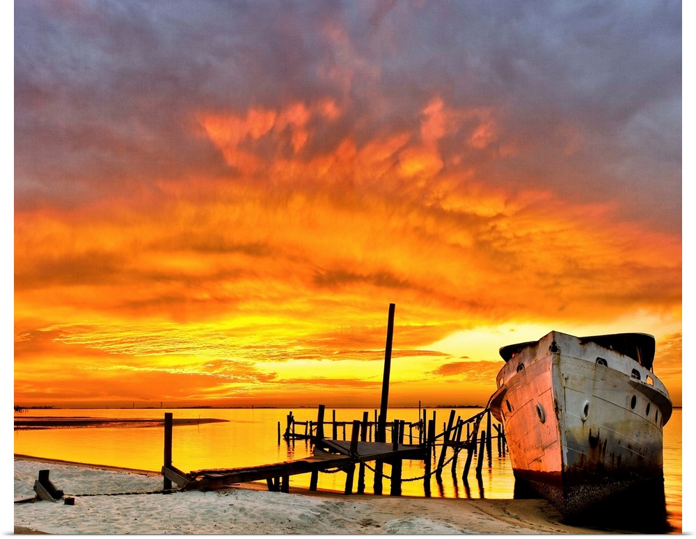 A dark red sunrise behind an old boat and broken pier. Landscape taken near Navarre Beach, Florida.
