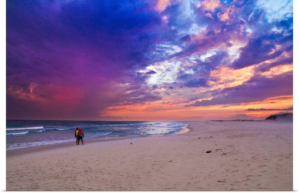 People walking on the beach during a pink and purple sunset along the Gulf Islands National Seashore.