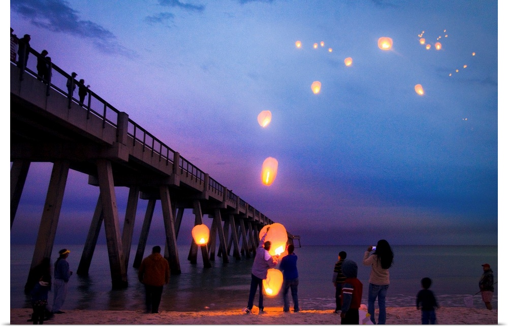 Blue seascape with people releasing paper lanterns over the sea.