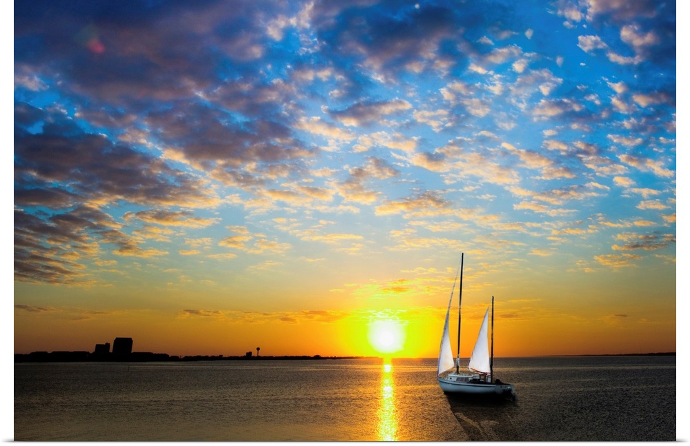 A sailboat sailing into the sun under a blue sky.