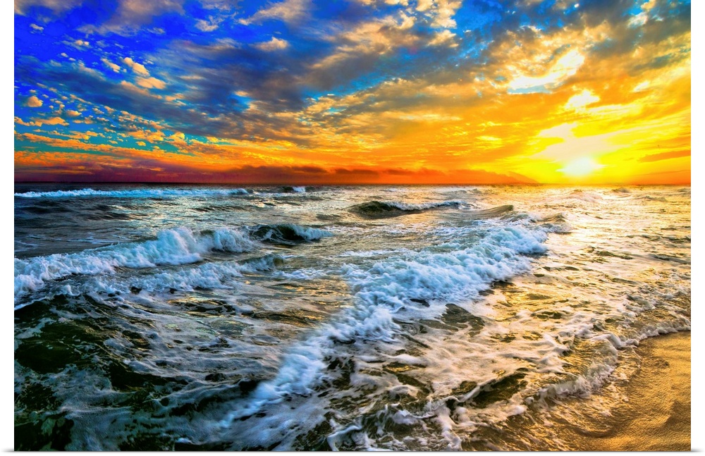 Beautiful ocean waves roll in front of a yellow orange and blue sunset. The sunset goes down into the beautiful blue ocean.