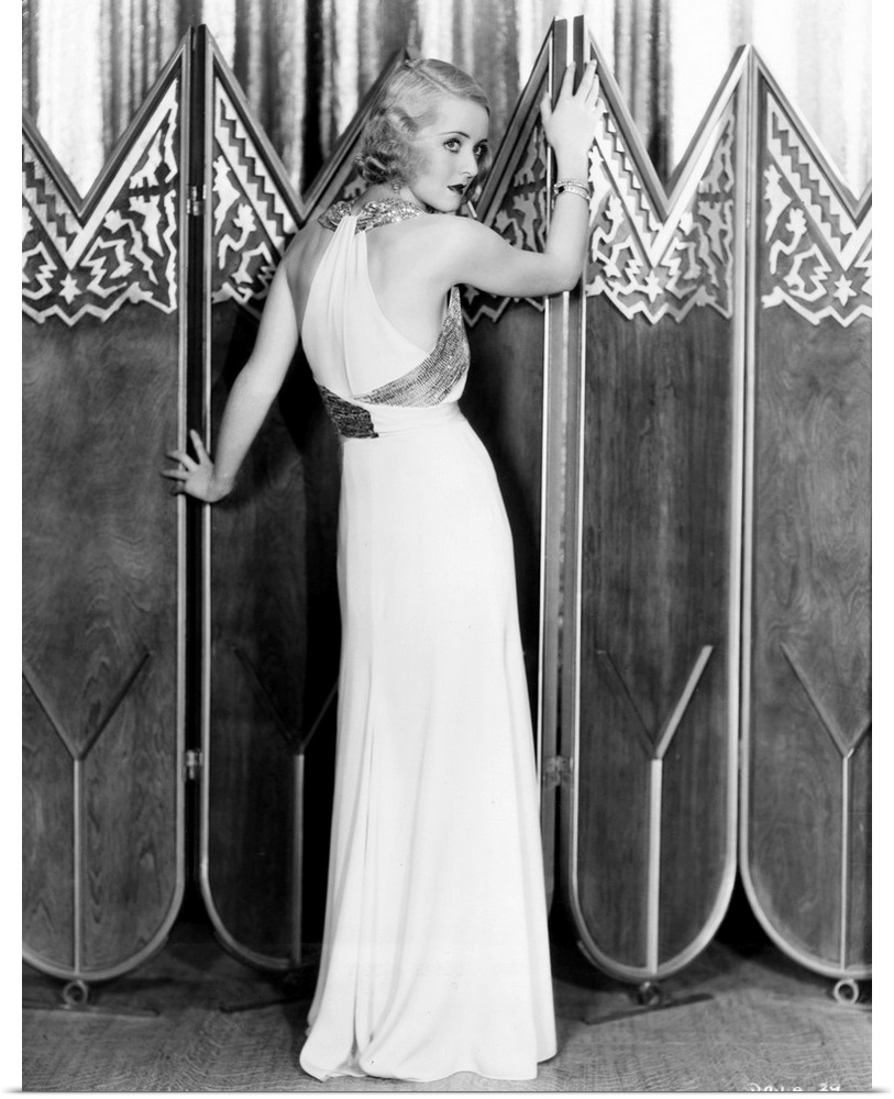 Bette Davis, modeling a white crepe evening gown with a silver sequined bodice sash, 1932.