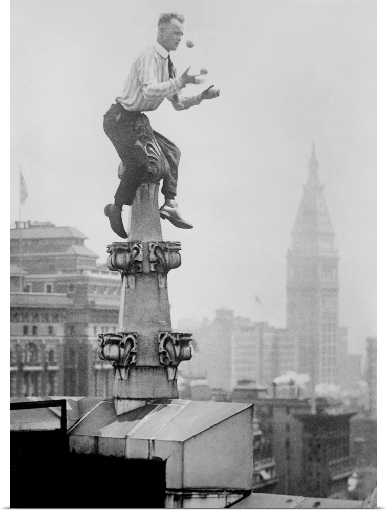 Human Fly' John 'Jammie' Reynolds juggles while balancing atop a roof decoration in New York City. In the distance is the ...