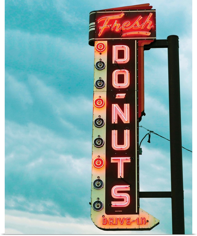 Photograph of a vintage 'Fresh Doughnut' neon sign with a cloudy blue sky in the background.