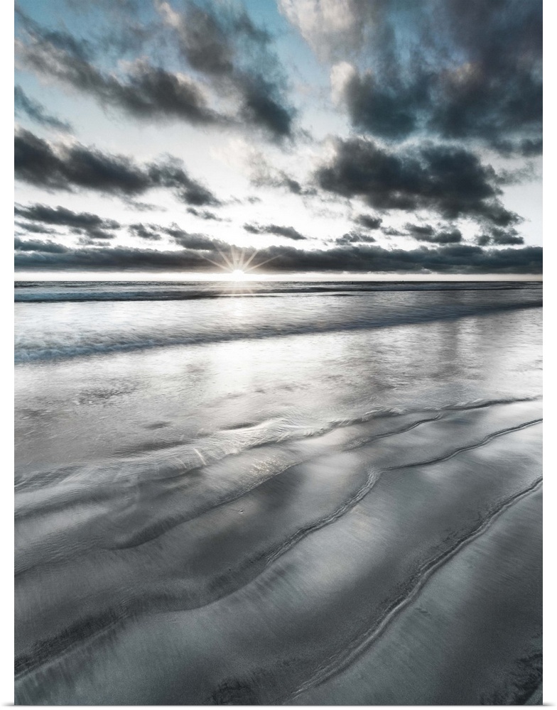 Black, blue, and white manipulated photograph of a seascape with the sun right on the horizon line.