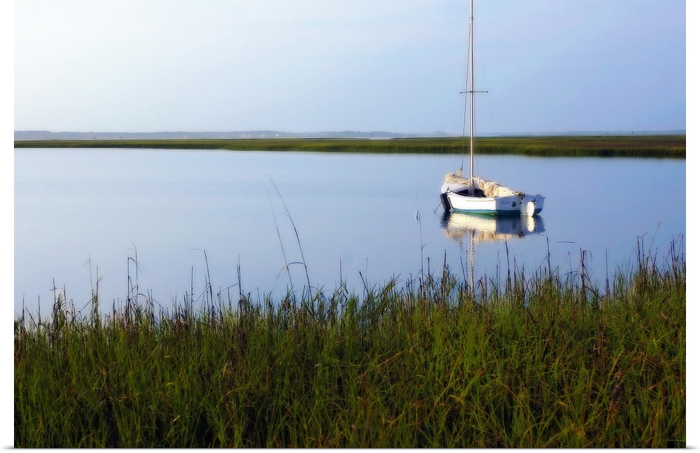 A landscape photograph of a sailboat anchored in still waters surrounded by marshy grasses on the shore.
