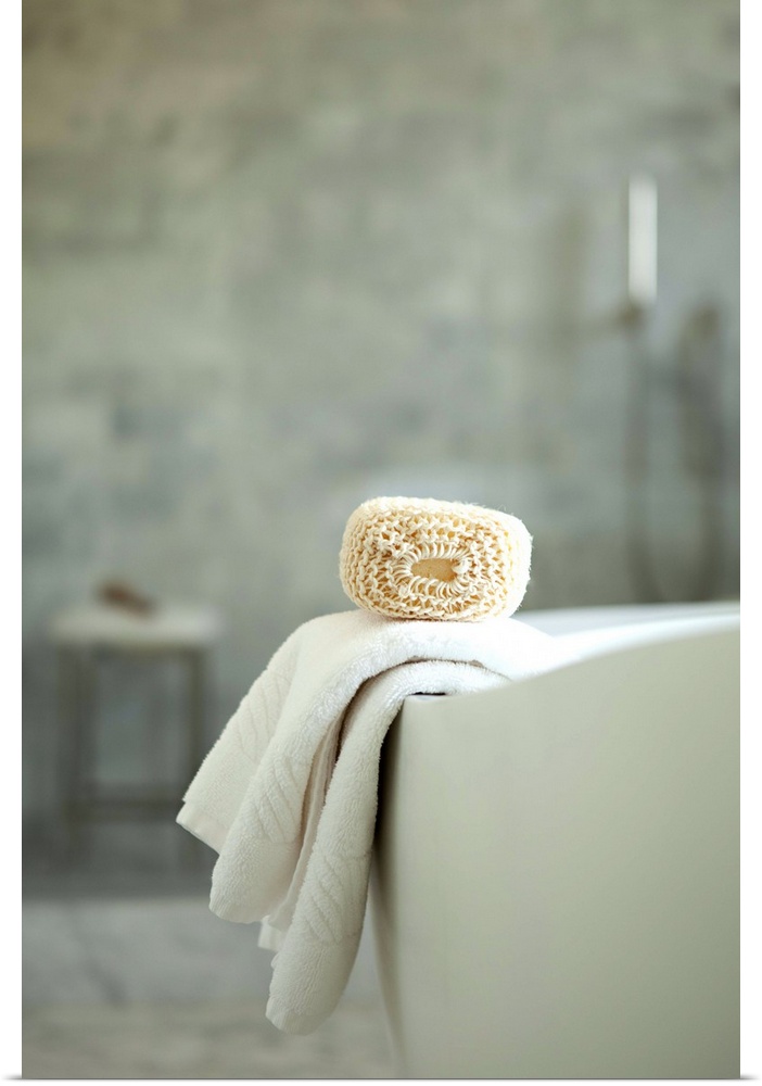 A loofah and towel resting on the edge of a bathtub.