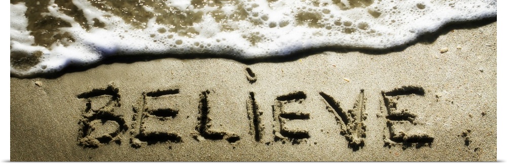The word "Believe" drawn in the sand near the ocean water.