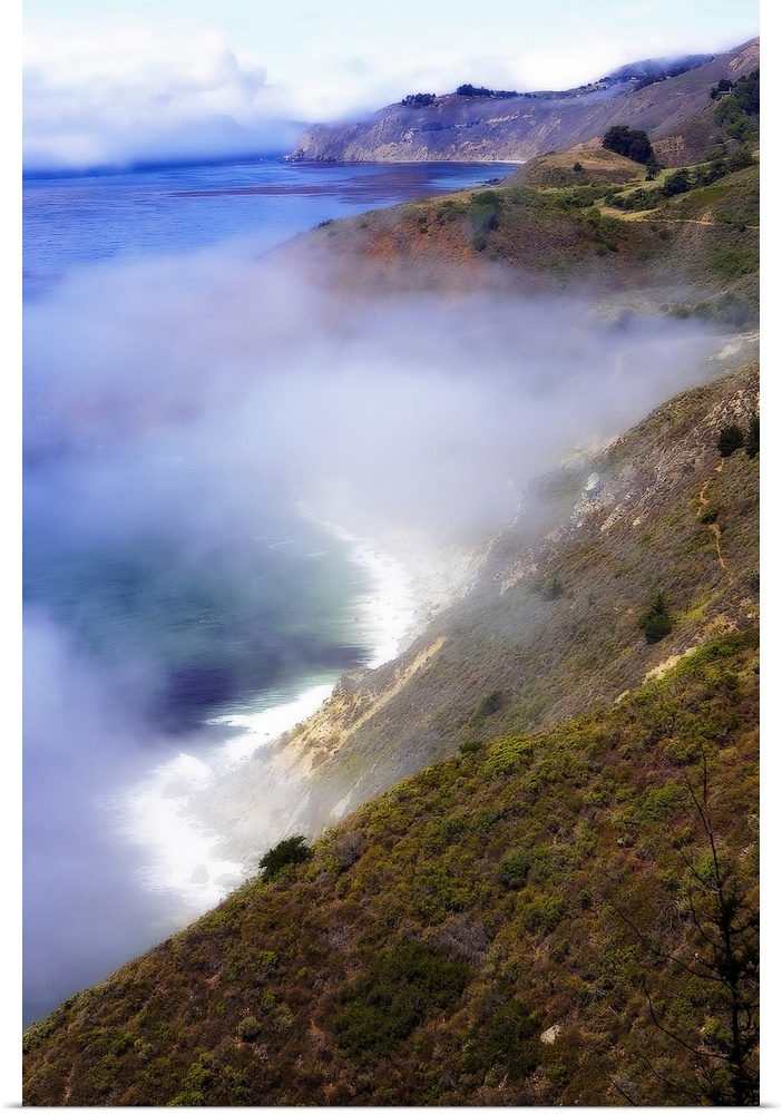 Photograph of fog rolling in off the California Big Sur ocean hitting the cliffs of the mountains that line the coast.