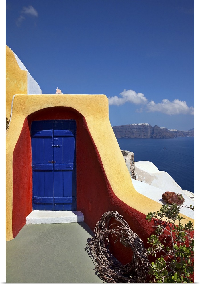 Close up vertical of deck with blue door and orange and red siding and ocean view in the village of Oia in Santorini, Greece
