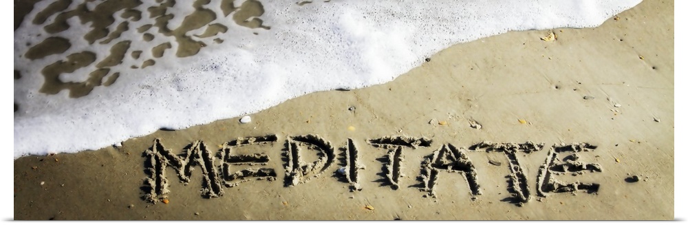The word "Meditate" drawn in the wet sand near ocean water.