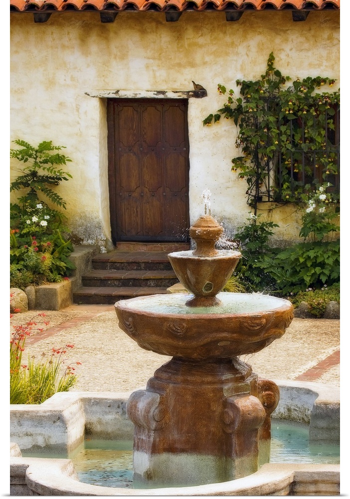 Photograph taken of a fountain sitting in front of a home with steps leading up to a wooden door. Foliage sits to either s...