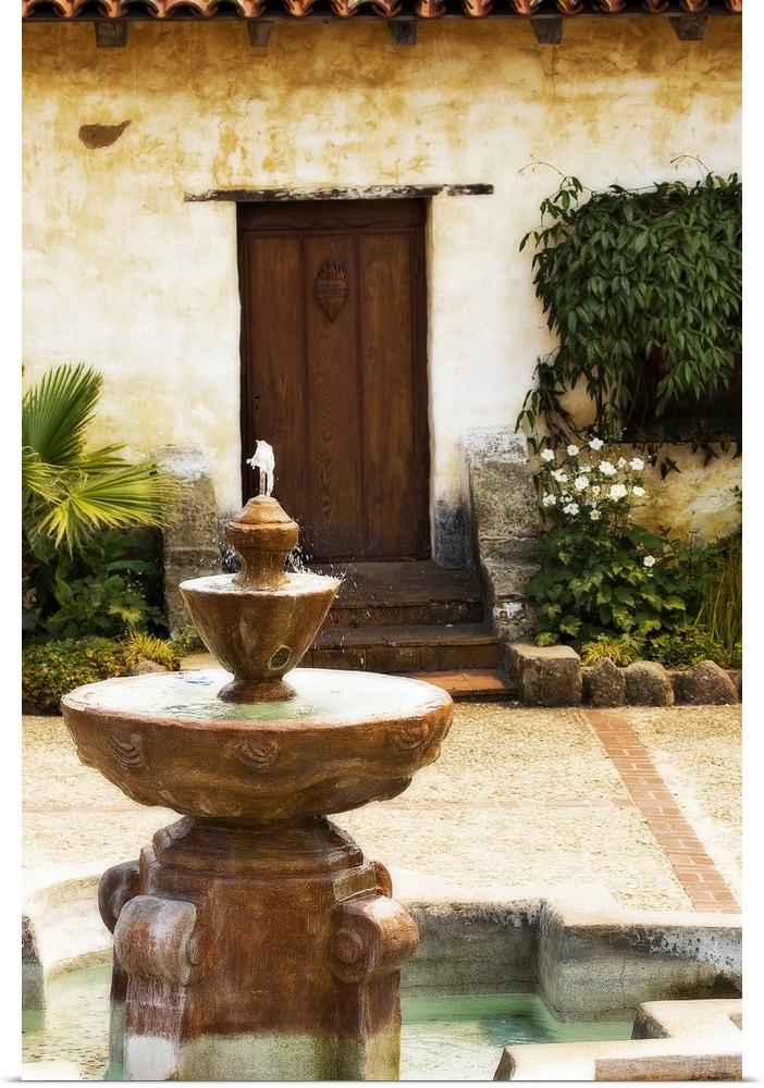 Photograph fountain with stone house and wooden door in background.