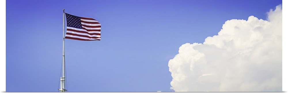 American flag flying high with large clouds in the blue sky.