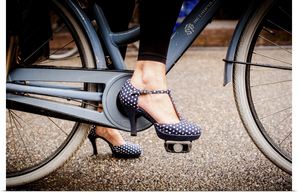 A woman in dotted high heels stepping onto the a bike pedal.
