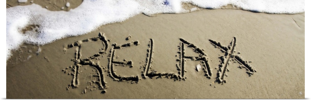 The word "Relax" drawn in the wet sand near ocean water.