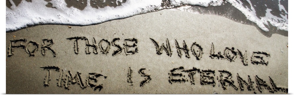A Bible verse drawn in the sand near the ocean water.
