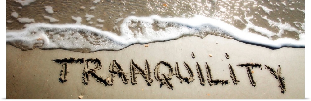 The word "Tranquility" drawn in the wet sand near ocean water.