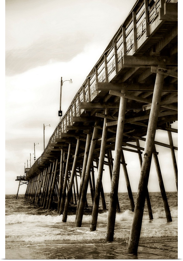 Photograph of dock stretching into ocean under cloudy sky.