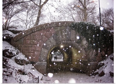 A couple walking under a bridge in New York City's Central Park on a snowy winter day.